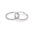 A pair of white gold hoop earrings with textured braided detailing and clear pavé-set stones along one side, displayed on a clean white background with a soft reflection.
