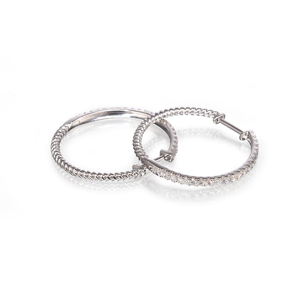 A pair of white gold hoop earrings with textured braided detailing and clear pavé-set stones along one side, displayed on a clean white background with a soft reflection.