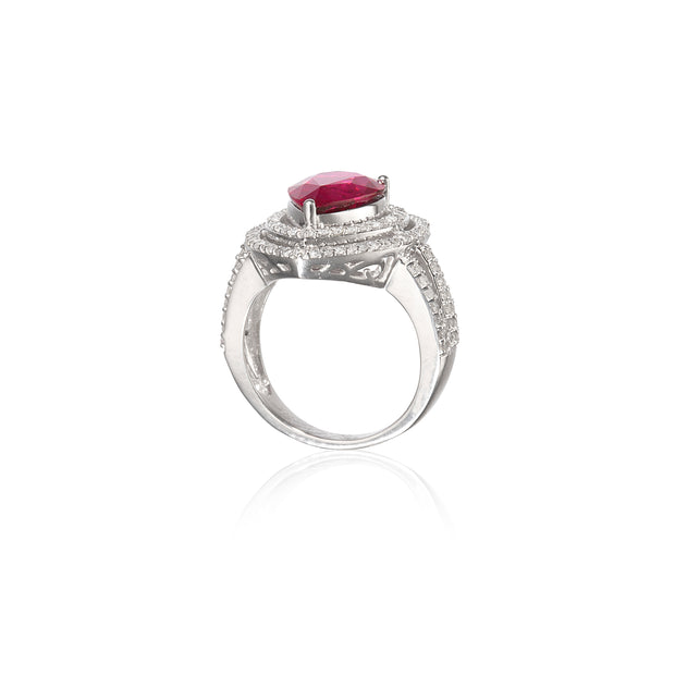 A white gold ring featuring a prominent oval-cut red gemstone in a prong setting, surrounded by a halo of small clear stones and an openwork patterned band, shown on a white background with a soft reflection.