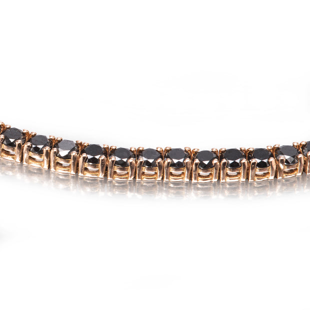 A close-up of a rose gold tennis bracelet with round black gemstones, shown against a white background with a soft reflection below.