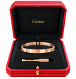 A Cartier Love bracelet in rose gold, displayed inside its signature red textured box with a black velvet interior. The box is open, showing the gold Cartier logo on the lid, and contains the bracelet along with its signature screwdriver tool.