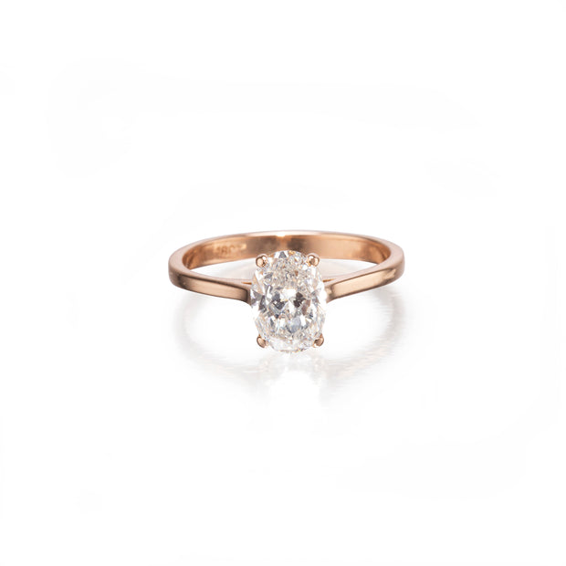 A rose gold engagement ring featuring an oval-cut diamond set in a four-prong setting, shown on a clean white background with a soft reflection.