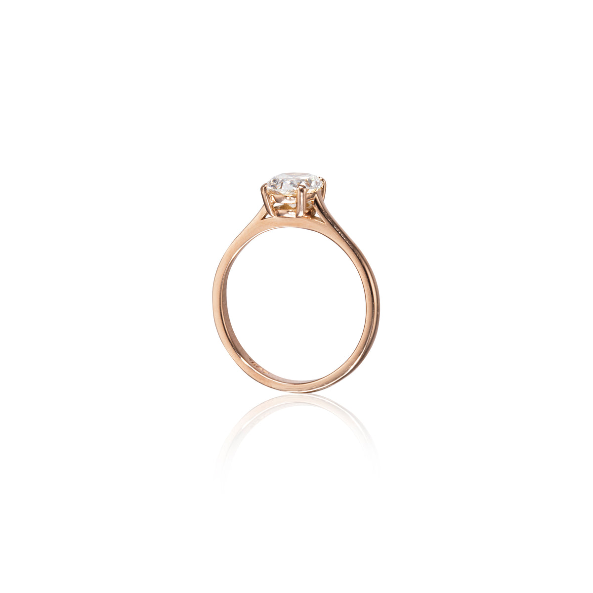 A rose gold solitaire ring with a round-cut clear gemstone in a four-prong setting, shown on a clean white background with a soft reflection below.