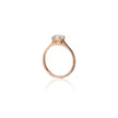 A rose gold solitaire ring with a round-cut clear gemstone in a four-prong setting, shown on a clean white background with a soft reflection below.