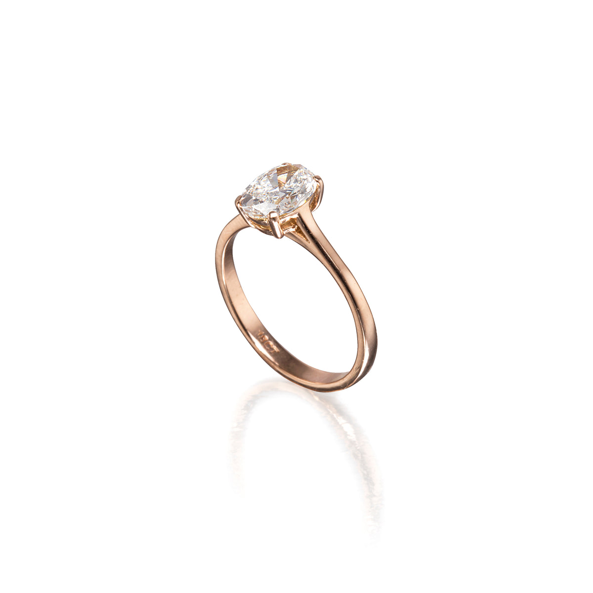 A rose gold engagement ring featuring a clear gemstone in a four-prong setting, shown on a clean white background with a soft reflection below.