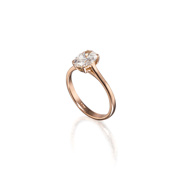 A rose gold engagement ring featuring a clear gemstone in a four-prong setting, shown on a clean white background with a soft reflection below.