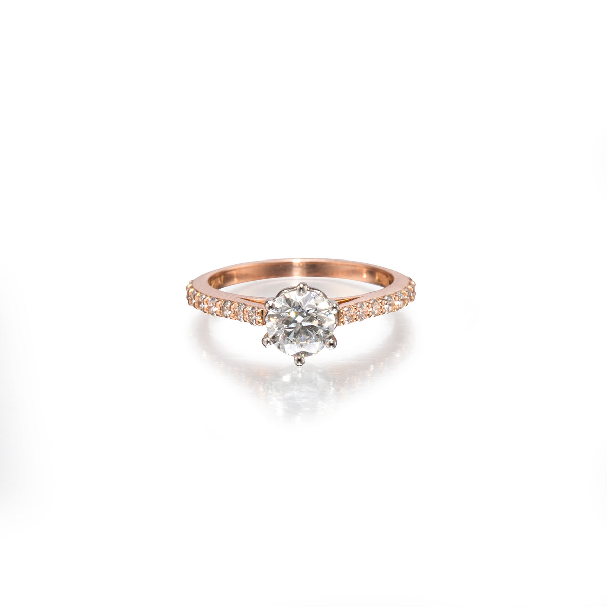 A rose gold engagement ring featuring a round-cut center stone in a prong setting, with a pavé band accented by small round stones, shown on a clean white background with a soft reflection.