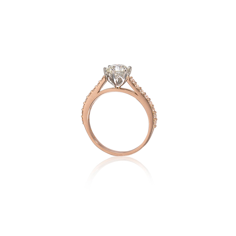A rose gold engagement ring featuring a round-cut diamond center stone in a four-prong setting, with small pavé diamonds, shown on a clean white background with a soft reflection.