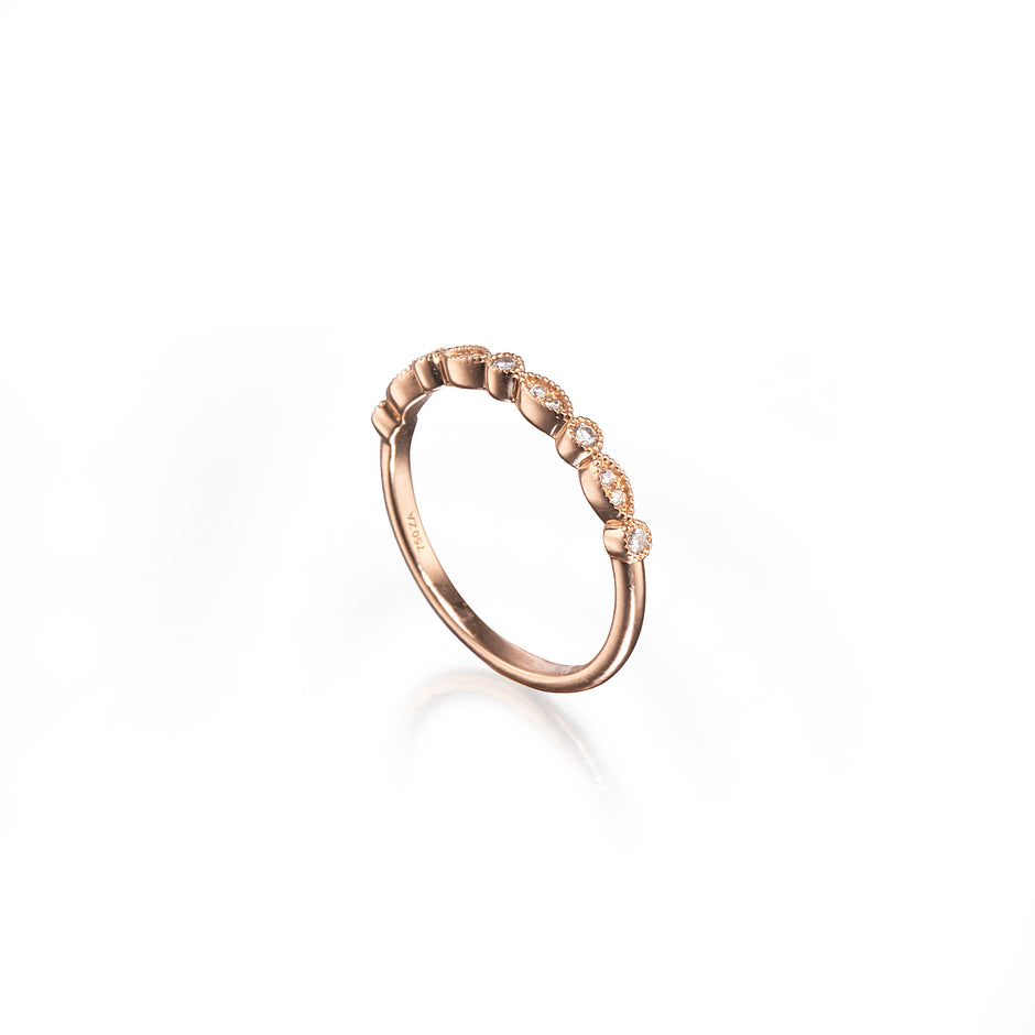 A rose gold eternity-style ring featuring a row of small clear gemstones set in a wavy, textured band, photographed on a clean white background with a soft reflection.