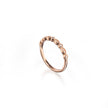 A rose gold eternity-style ring featuring a row of small clear gemstones set in a wavy, textured band, photographed on a clean white background with a soft reflection.