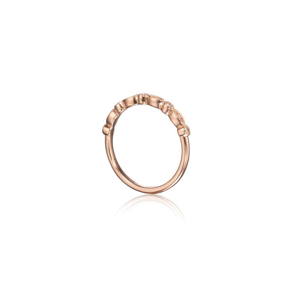 A rose gold ring with a textured, beaded outer band and small clear stones set along the top, shown on a clean white background with a soft reflection below.