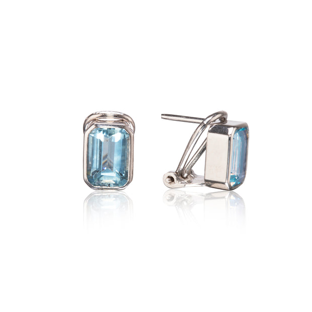 A pair of stud earrings featuring rectangular light blue gemstones in a bezel setting, shown from both front and side angles on a white background with a soft reflection.