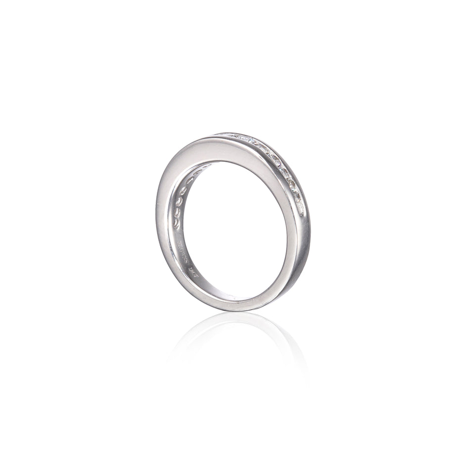 A polished white gold band ring with a row of small clear stones set along the outer edge, shown on a clean white background with a soft reflection below.