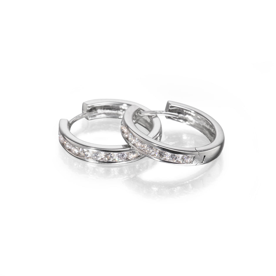 A pair of white gold huggie hoop earrings with a channel-set row of clear cubic zirconia stones, displayed on a clean white reflective surface.