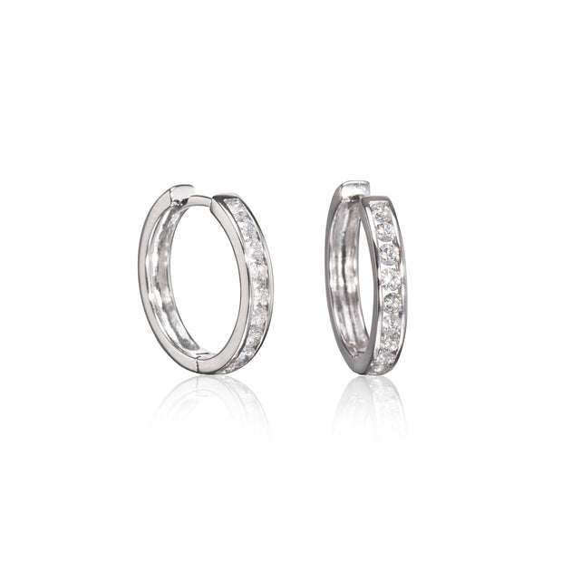 A pair of white gold hoop earrings with a channel setting of clear stones, displayed on a clean white background with a soft reflection below.