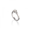 A white gold solitaire engagement ring with a round brilliant-cut diamond set in a four-prong setting, shown on a clean white background with a soft reflection below.