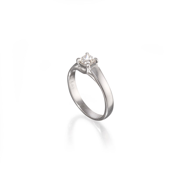 A white gold solitaire engagement ring with a round brilliant-cut diamond set in a four-prong setting, shown on a clean white background with a soft reflection below.