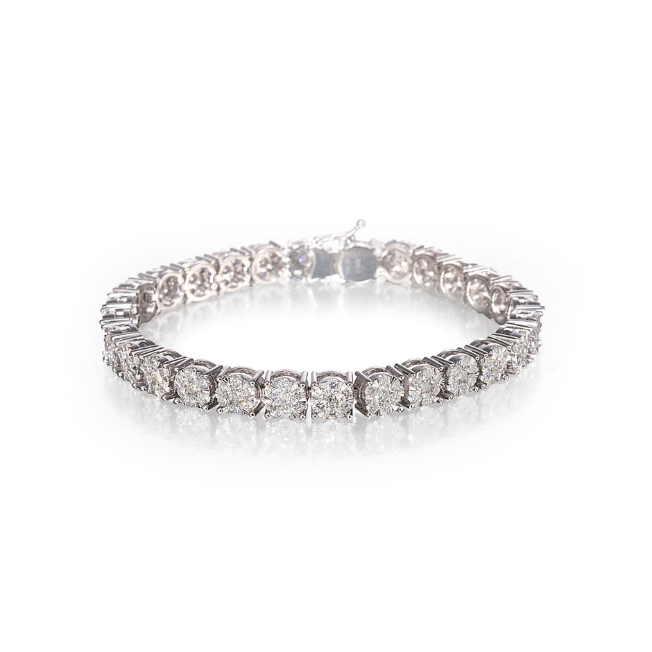 A white gold tennis bracelet with round-cut clear stones, photographed on a reflective white surface against a white background.