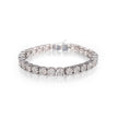 A white gold tennis bracelet with round-cut clear stones, photographed on a reflective white surface against a white background.