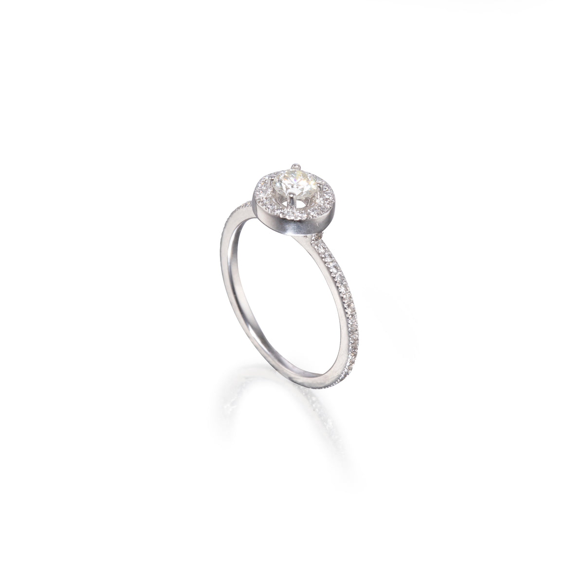 A white gold engagement ring featuring a round-cut center stone surrounded by a halo, with a pavé-set band, shown on a white background with a soft reflection.