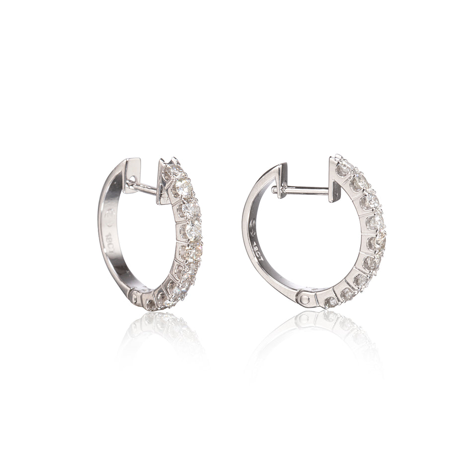 A pair of white gold hoop earrings with clear pavé-set stones, shown from the side on a white background with a soft reflection below.