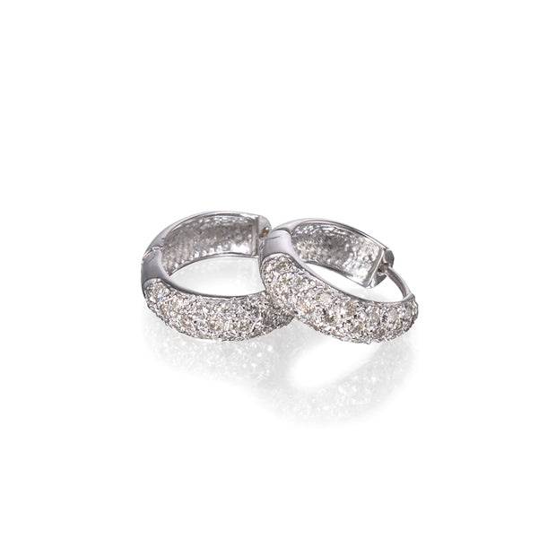 A pair of white gold huggie hoop earrings paved with clear cubic zirconia stones, displayed on a clean white reflective surface.