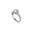A white gold ring featuring a large round-cut clear center stone and a row of smaller clear stones along the band, shown on a plain white background with a soft reflection below.