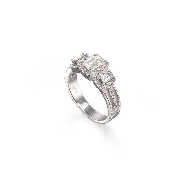 A white gold ring featuring a row of baguette-cut clear stones and smaller accent stones, photographed on a clean white background with a soft reflection.