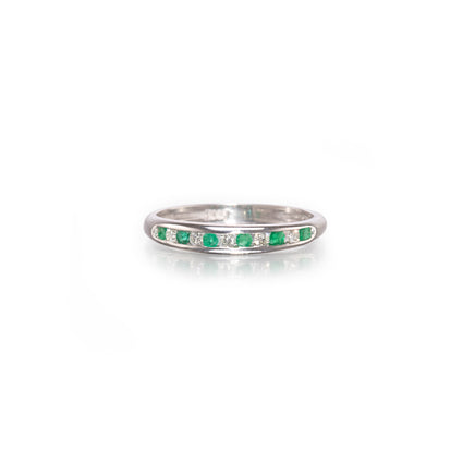 A white gold band ring featuring a row of small green emerald-cut gemstones and clear round stones, shown on a clean white background with a soft reflection.