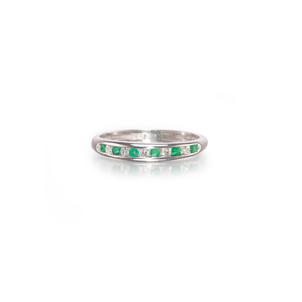 A white gold band ring featuring a row of small green emerald-cut gemstones and clear round stones, shown on a clean white background with a soft reflection.
