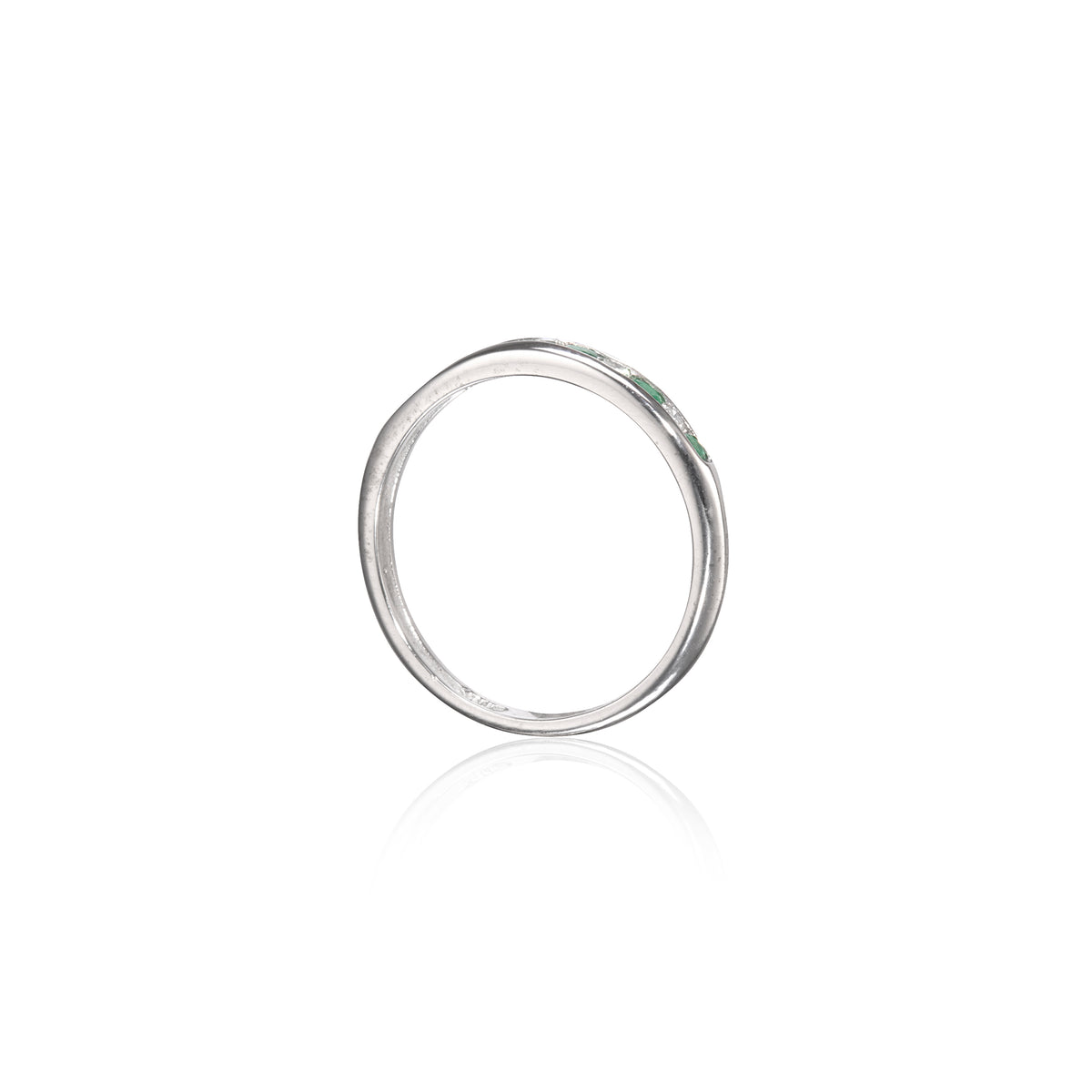 A slim white gold band ring with a small green gemstone accent on the right side, shown against a plain white background with a soft reflection below.
