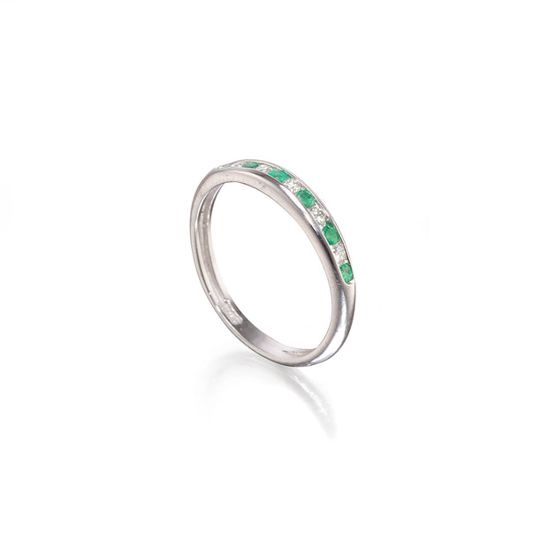 A white gold band ring featuring a row of small green emerald-cut gemstones and clear accent stones, shown on a clean white background with a soft reflection.