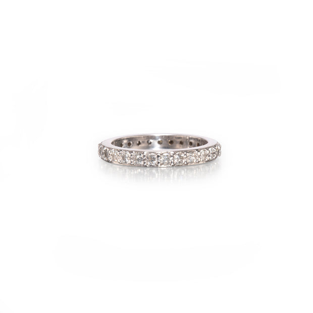 A diamond eternity band ring in a silver-colored metal setting, shown on a clean white background with a soft reflection underneath.