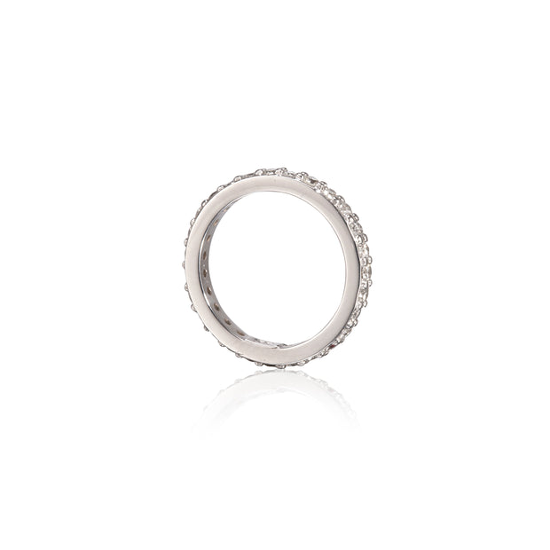 A white gold  eternity ring with small clear stones set all around the band, shown on a clean white background with a soft reflection below.