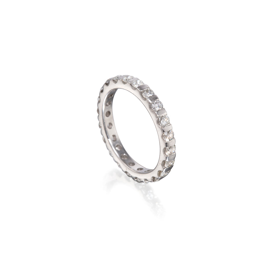 A white gold eternity ring with a full beaded band set with small clear round gemstones, shown on a clean white background with a soft reflection.