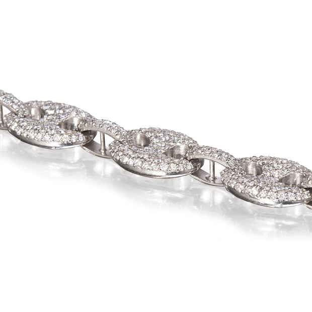 A close-up of a white gold chain bracelet featuring oval links paved with small clear stones, set against a bright white background with a soft reflection.