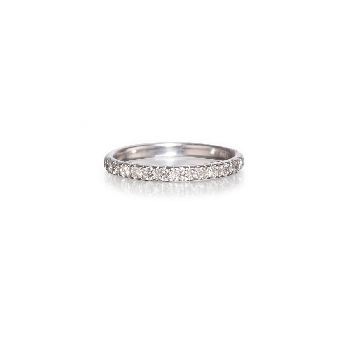 A thin white gold band ring paved with small clear round stones, centered on a clean white background with a soft reflection below.