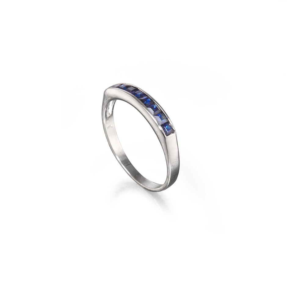 A white gold band ring featuring a row of small square-cut blue gemstones, shown on a clean white background.