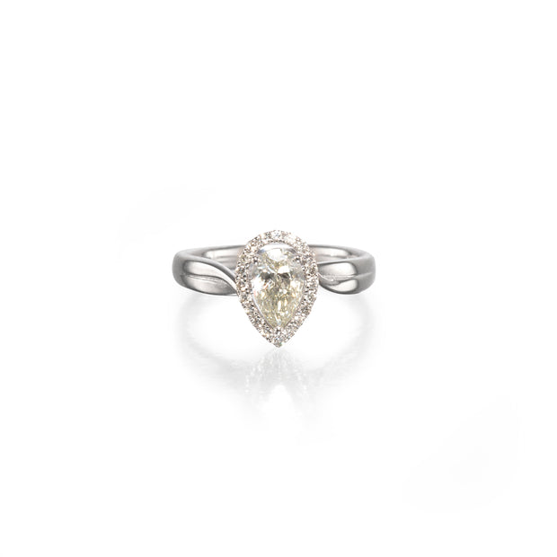 A pear-shaped diamond ring with a halo setting and a polished white gold band, centered on a clean white background with a soft reflection below.