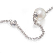 A close-up of a white gold chain necklace featuring a large, lustrous white pearl and a small round silver charm with a tiny clear stone, set against a clean white background.