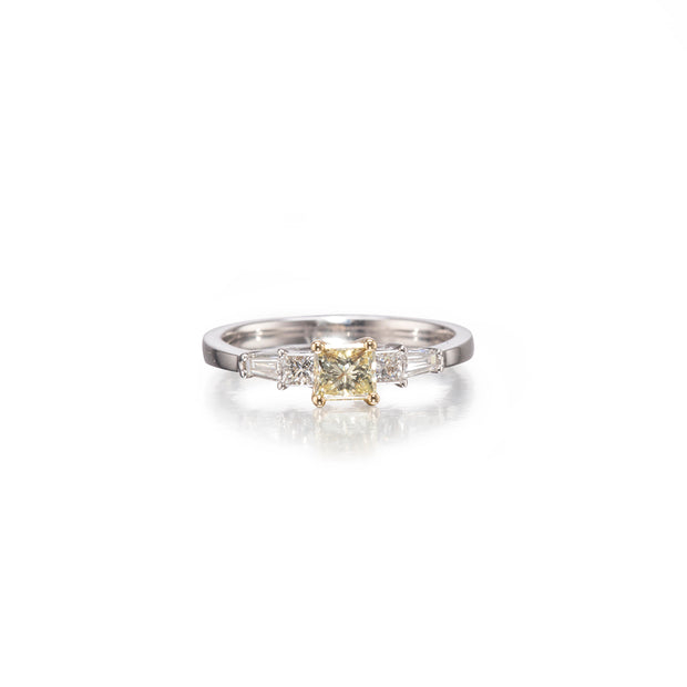 A white gold band ring featuring a central yellow cushion-cut diamond surrounded by three baguette-cut diamonds, set against a clean white background with a soft reflection.