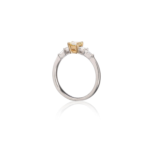 A white gold ring with a yellow gold center stone and small clear accent stones on either side of the band, shown on a white background with a soft reflection below.