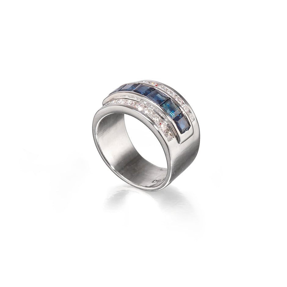 A white gold ring featuring a curved top set with dark blue rectangular stones on one side and small clear round stones on the other, photographed on a clean white background.