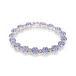 A white gold tennis bracelet featuring round light blue tanzanite gemstones and small clear accent stones, displayed on a clean white background with a soft reflection.