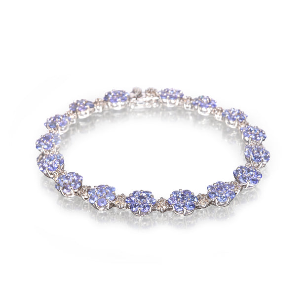 A white gold tennis bracelet featuring round light blue tanzanite gemstones and small clear accent stones, displayed on a clean white background with a soft reflection.