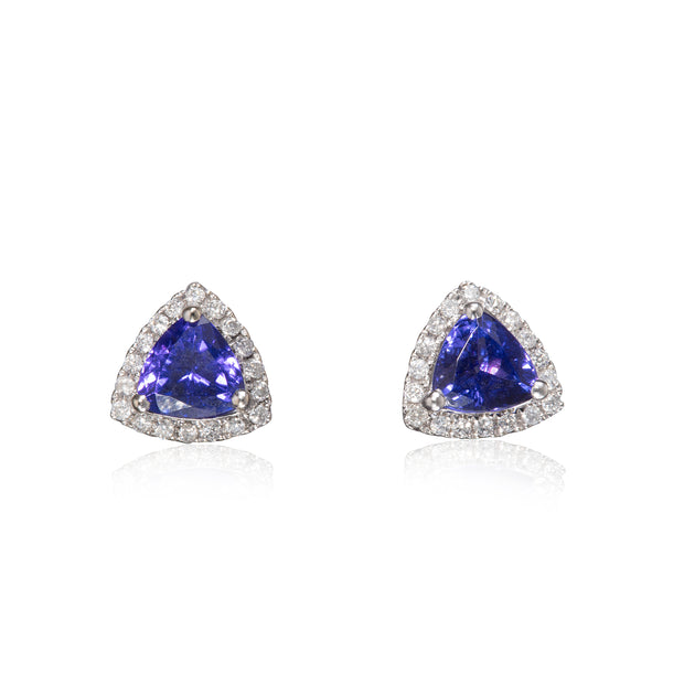 A pair of triangular stud earrings featuring a central blue tanzite gemstone surrounded by a halo of small clear stones in a white gold setting, shown on a white background with a soft reflection.