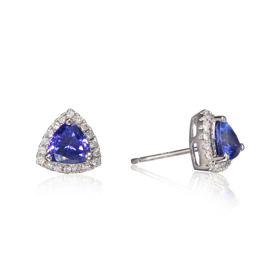 A pair of triangular stud earrings featuring a central blue sapphire stone surrounded by a halo of small clear stones in a white gold setting, shown on a white reflective background.