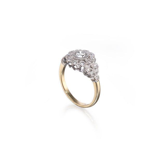 A vintage-style two-tone ring featuring a yellow gold band and a silver-toned diamond cluster setting, shown on a clean white background with a soft reflection.