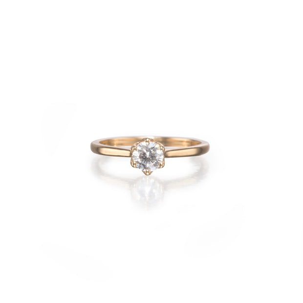 A single solitaire engagement ring featuring a round brilliant-cut diamond set in a yellow gold four-prong setting on a slim yellow gold band, shown on a reflective white surface.