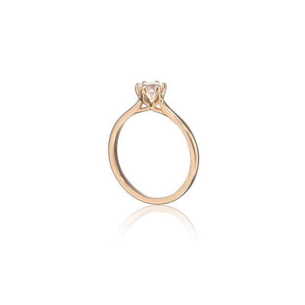 A yellow gold solitaire engagement ring with a round brilliant-cut diamond set in a four-prong setting, shown on a clean white background with a soft reflection below.